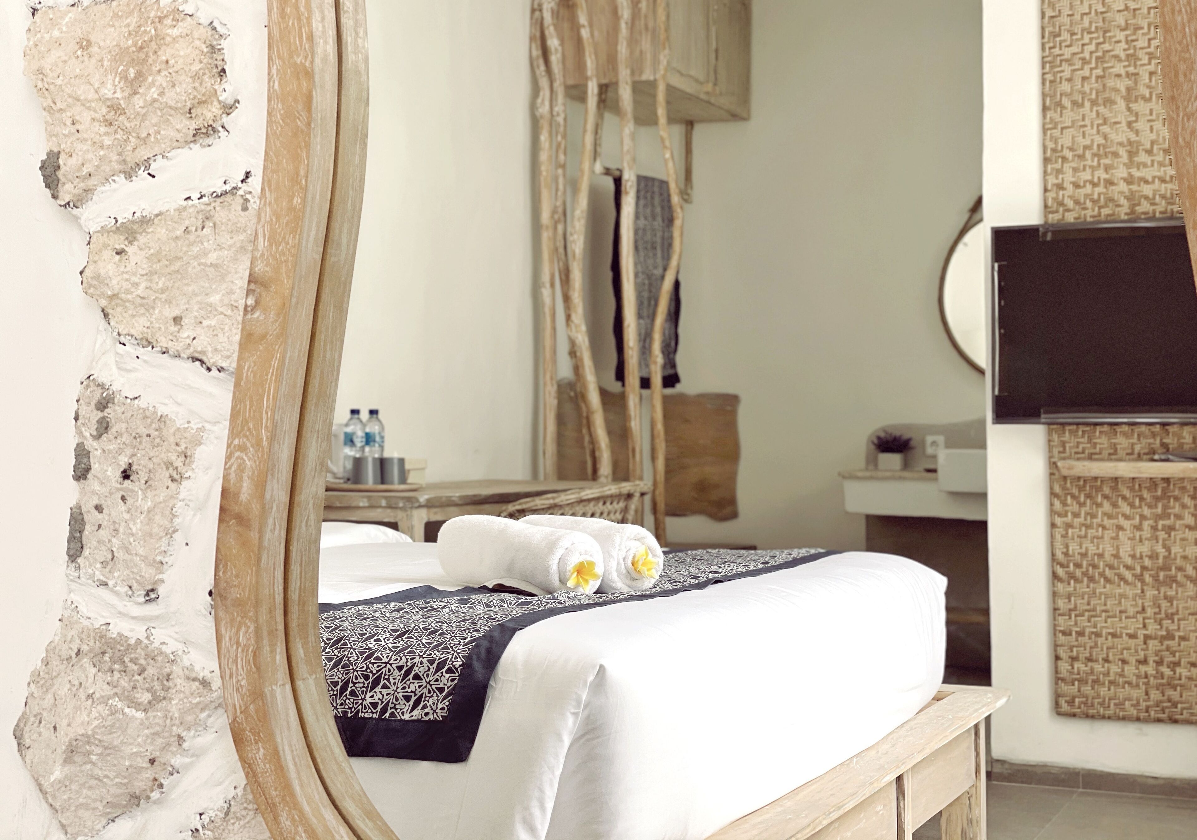 A bedroom with a stone wall, a wooden bed frame, a large mirror, and a bedside table with a bottle.