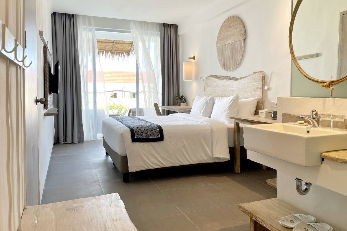 Ein Hotelzimmer mit Bett, Nachttisch und einem Badezimmer mit Waschbecken und Spiegel.