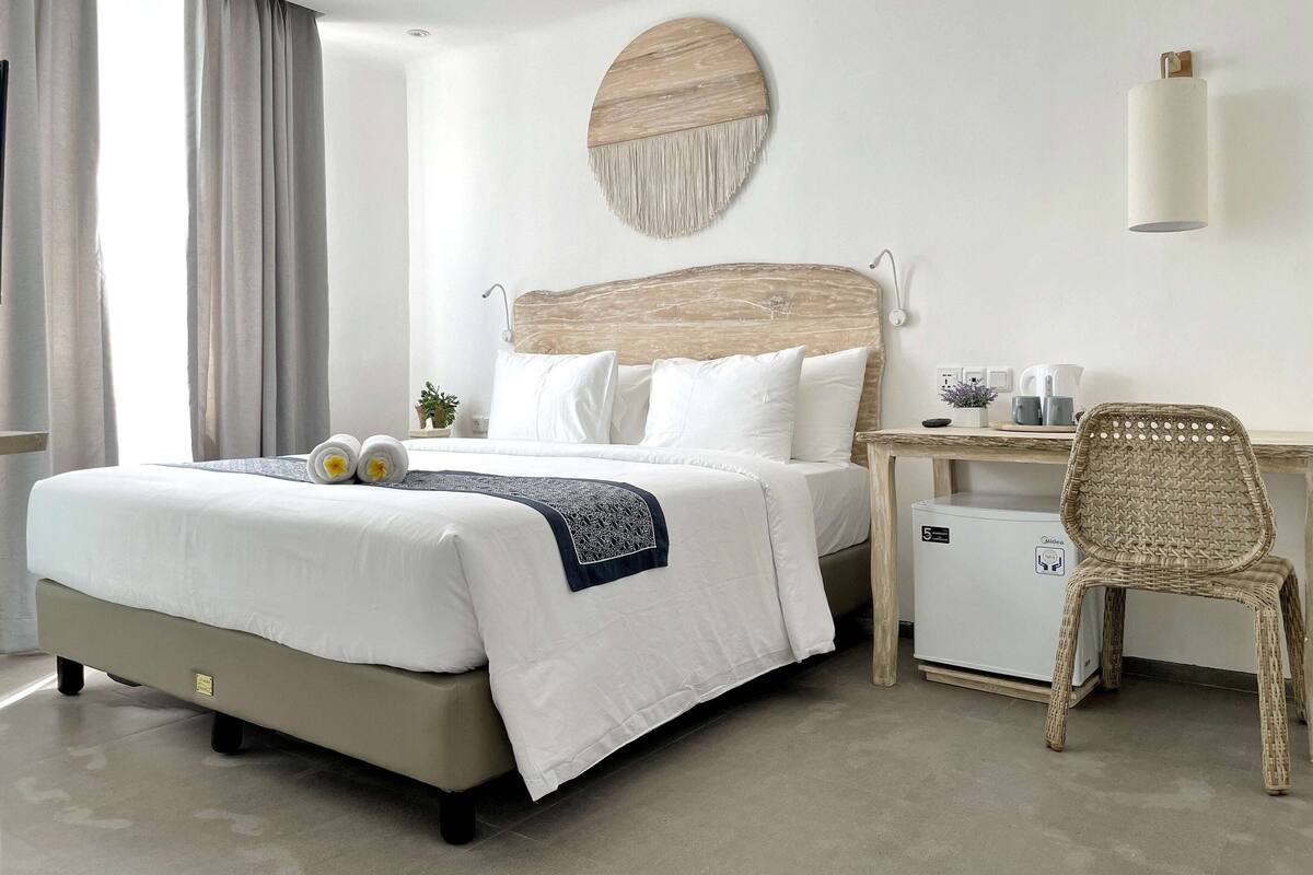 Ein Hotelzimmer mit Bett, Nachttisch, Sessel und kleinem Kühlschrank.