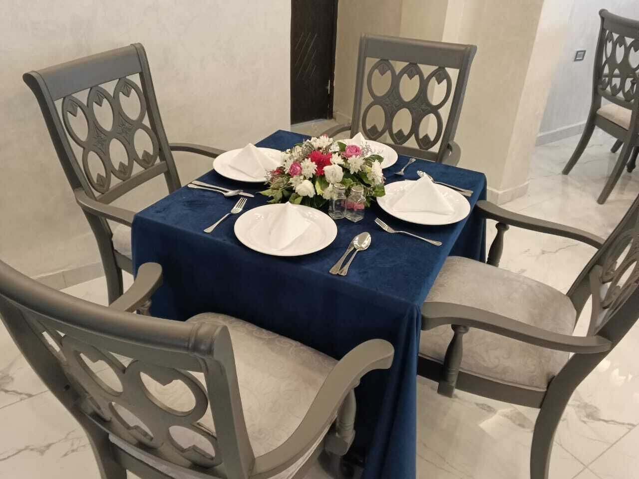 Une table à manger dressée pour quatre personnes, avec une nappe bleue, des assiettes blanches, des couverts en argent et un centre de table floral.