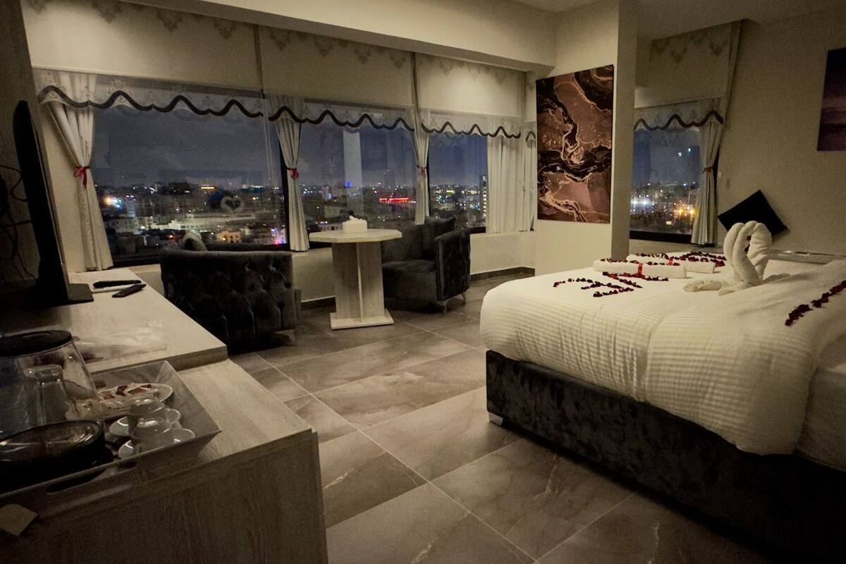 A modern hotel room with a large bed, a small table, and a view of the city at night.