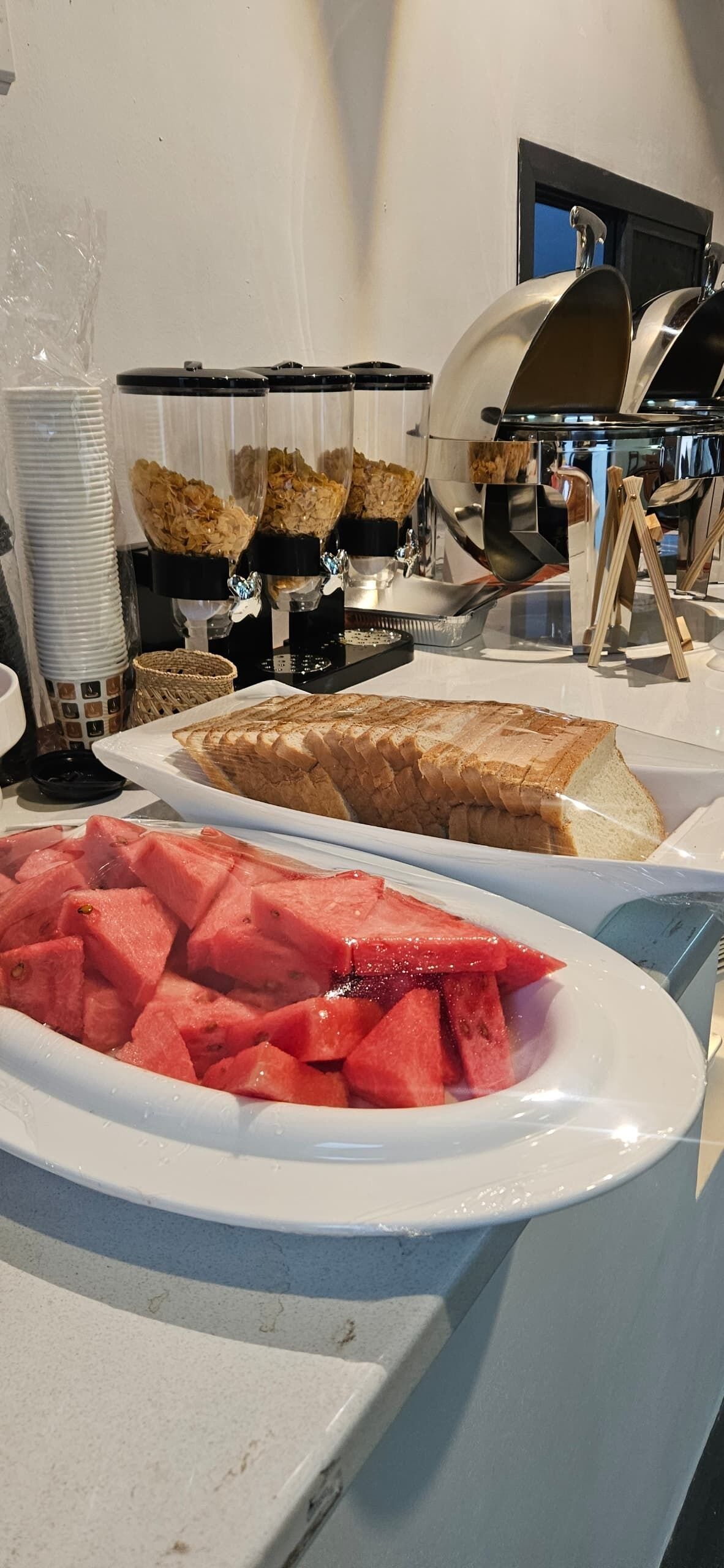 A buffet with sliced bread, watermelon, and cereal bowls.