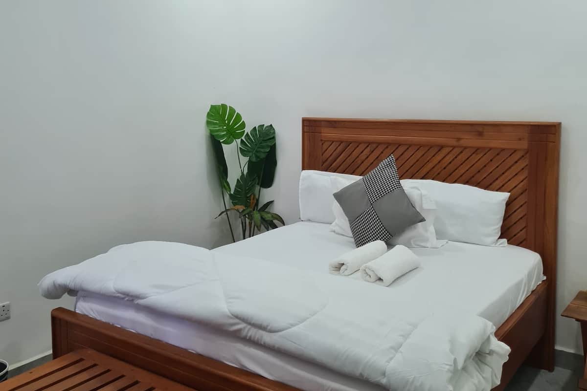 A neatly made bed with white bedding and a wooden headboard, a small wooden bench, and a potted plant beside the bed.