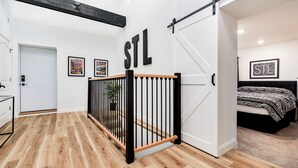 Ein modernes Interieur mit Holzboden, einer Schiebetür mit der Aufschrift „STL“ und einem Bett mit einem gemusterten Überwurf.