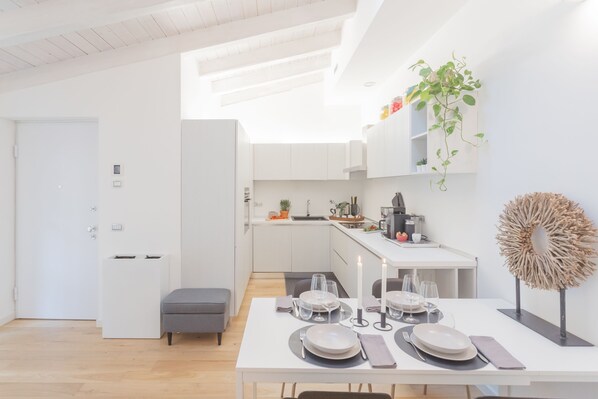 A modern kitchen with white cabinetry, a dining area with a white table set for four, and a plant on the wall. - Palazzo Tatti in Como (Como)