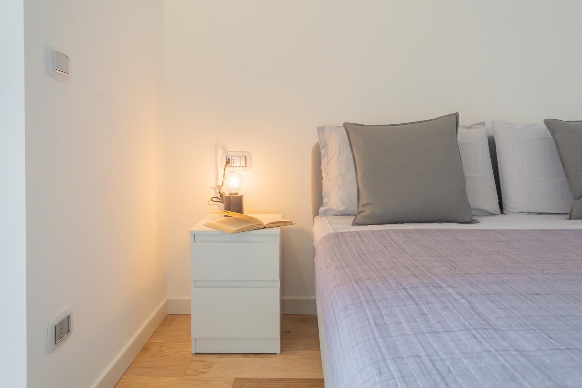 A bedroom with a bed, bedside table, and a wall socket.