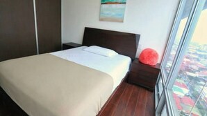 A bedroom with a bed, a nightstand, a red pillow, a painting on the wall, and a view of the city through a large window. - Apartamento Amoblado Elegante San José Costa Rica (San José)