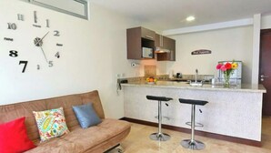 A modern kitchen with a bar area, a clock on the wall, and a sofa with colorful cushions. - Apartamento Amoblado Elegante San José Costa Rica (San José)