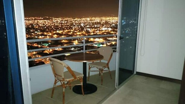 A balcony with a table and two chairs, overlooking a cityscape at night. - Apartamento Amoblado Elegante San José Costa Rica (San José)