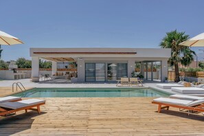 Uma área de piscina moderna ao ar livre, com deck de madeira, espreguiçadeiras e guarda-sóis.