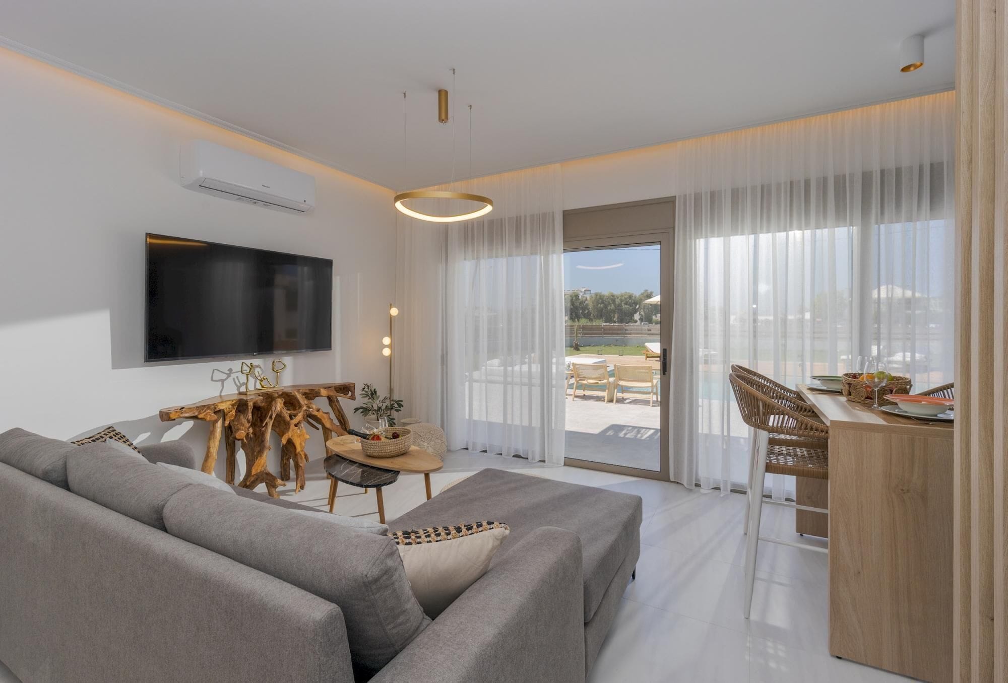 A modern living room with a sofa, a wooden coffee table, a TV mounted on the wall, and a dining area with a table and chairs.