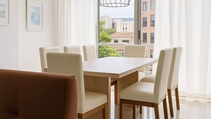 Ein moderner Essbereich mit einem Holztisch, sechs Stühlen, großen Fenstern mit weißen Vorhängen und einer Hängelampe.