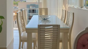 A dining area with a glass table and white chairs, a hanging light fixture, and a view of buildings and mountains through large windows. - Nice view of the mountains in the north of Cali (Cali)