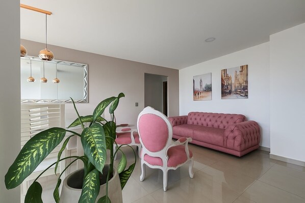 Ein modernes Wohnzimmer mit einem rosafarbenen Sofa, einem weißen Sessel und einer großen Pflanze.