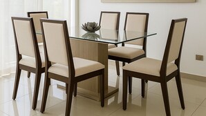 A dining area with a glass table surrounded by six chairs, a decorative bowl, and three pendant lights.