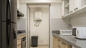 A modern kitchen with a refrigerator, microwave, and stove. There is a trash bin and a water heater visible.