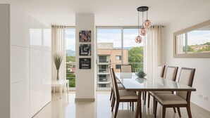 A modern dining area with a glass table and chairs, a vase with plants, and a cityscape view through large windows.