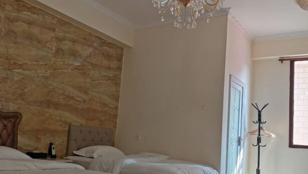A hotel room with a stone accent wall, a chandelier, a coat rack, and a bed with white bedding. - Shangxi Apartment (Zhaoqing)