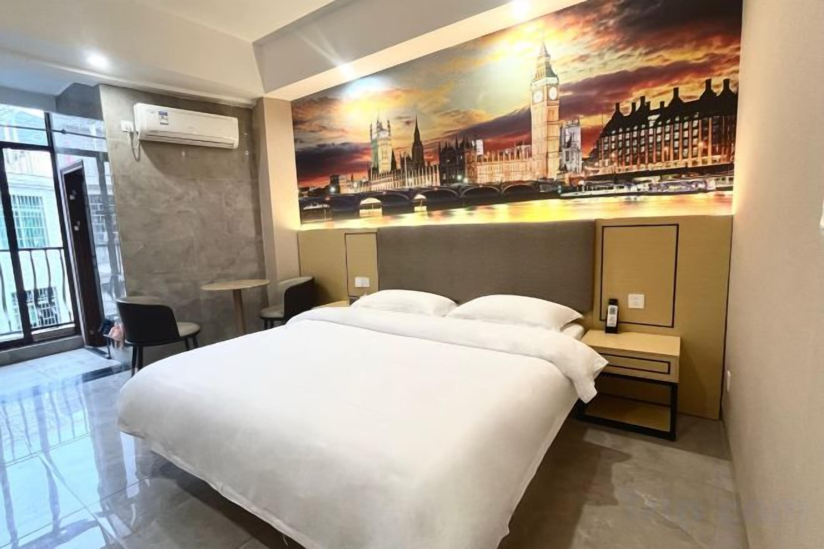 A hotel room with a large bed, a desk, a chair, and a painting of a cityscape.