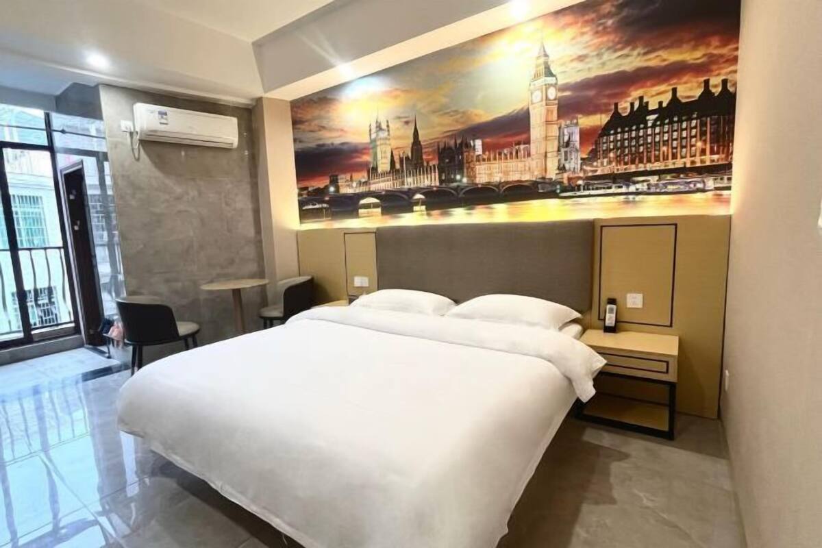 A hotel room with a large bed, a desk, a chair, and a view of a cityscape painting.
