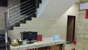 A reception desk with a computer, a piggy bank, and a small table. A staircase is visible in the background. - Shangxi Apartment (Zhaoqing)