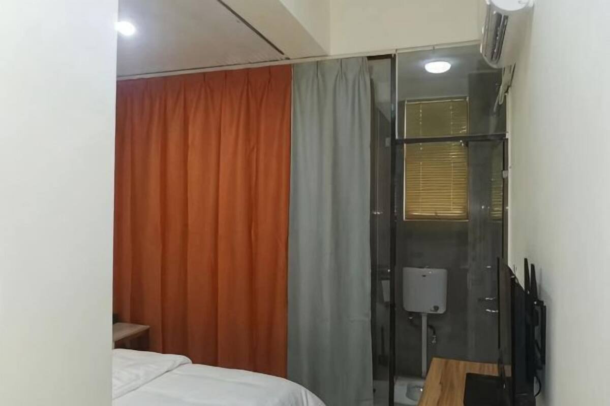 A hotel room with a bed, a desk, a chair, a shower area, and a toilet.