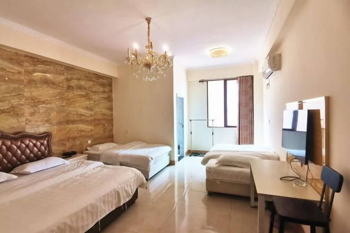 A hotel room with two beds, a chandelier, a desk with a chair, and a television.