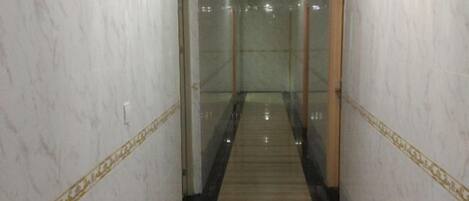 A marble hallway with a central carpeted walkway, glass doors, and a chandelier.