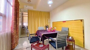 A dining area with a table set for four, chairs, a small table with a bottle and flowers, and a yellow curtain. - Shangxi Apartment (Zhaoqing)