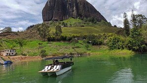 A boat on a calm river with a large rock formation in the background. - Lakeview Cabin with Jacuzzi in Guatapé (Guatapé)