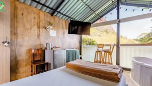 A room with a bed, a TV, a small table with a chair, and a hot tub. - Lakeview Cabin with Jacuzzi in Guatapé (Guatapé)