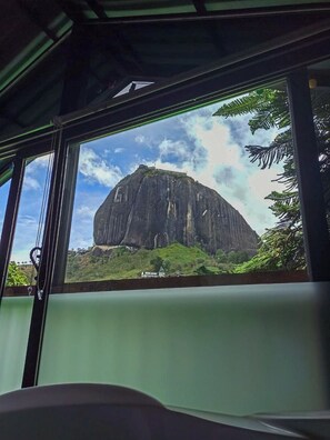 A view from inside a vehicle, looking out through a window at a large rock formation with a small building in the foreground. - Lakeview Cabin with Jacuzzi in Guatapé (Guatapé)