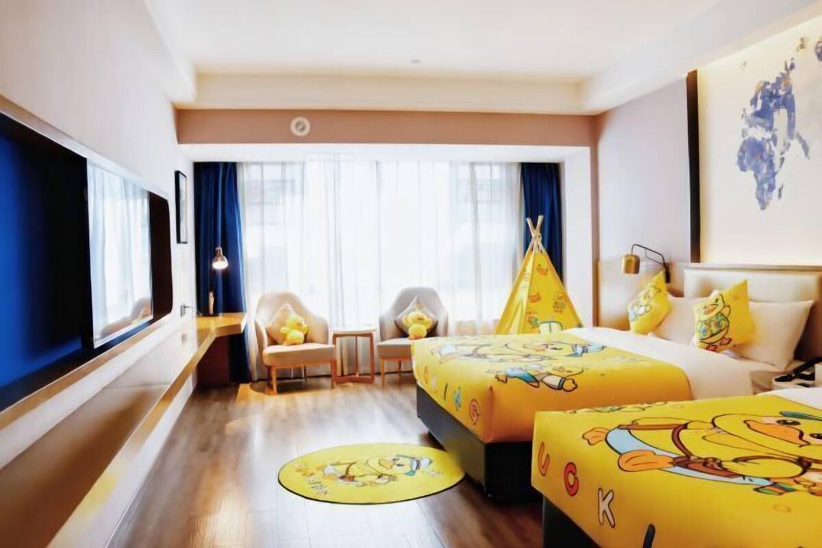 A hotel room with two beds, a large window, a chair, a desk, and a wall-mounted TV.