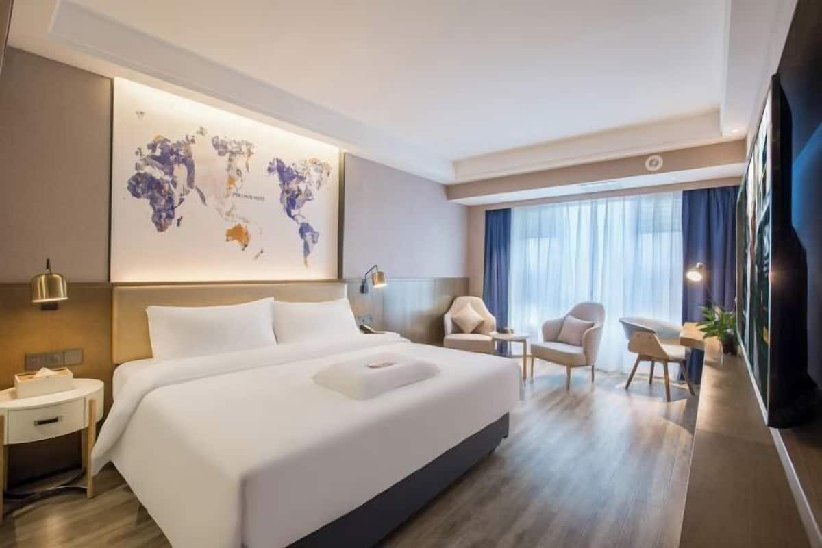 A modern hotel room with a large bed, a desk, a chair, and a world map on the wall.
