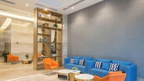 A modern lobby with a blue sofa, orange chairs, and a bookshelf. - Guiyi Hotel (Guiyang Guanshanhu District Southwest International Trade City Store) (Guiyang)