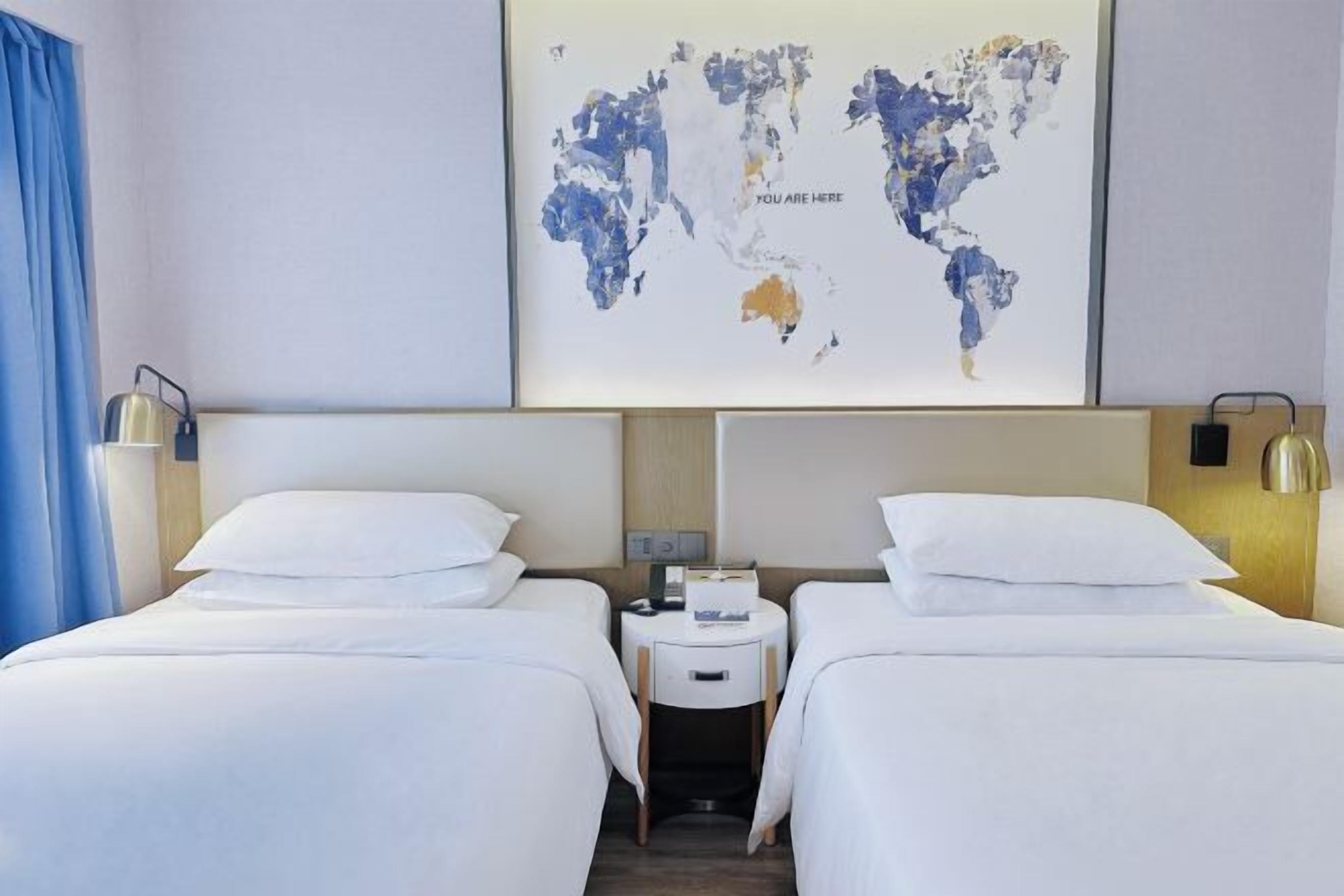 A hotel room with two beds, a small table, and a world map on the wall.