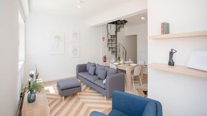 A modern living room with a sofa, a dining table, and a staircase leading to another room. - Liiiving in Porto - Downtown Balcony Apartment (Porto)