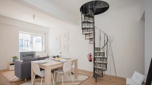 A modern living room with a spiral staircase, a dining area with a table and chairs, and a sofa. - Liiiving in Porto - Downtown Balcony Apartment (Porto)
