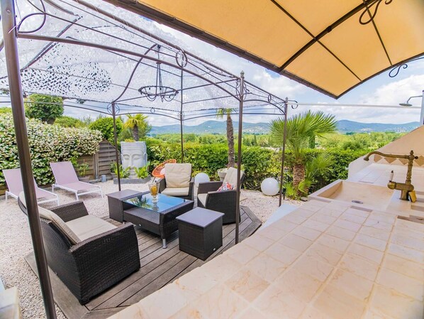 Relax in a serene outdoor space with wicker lounge chairs and a small table, surrounded by lush greenery and a distant view.