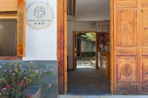 A wooden entrance with a sign, a pathway leading inside, and a potted plant with pink flowers. - Huachengju View Guesthouse (Jianshui)