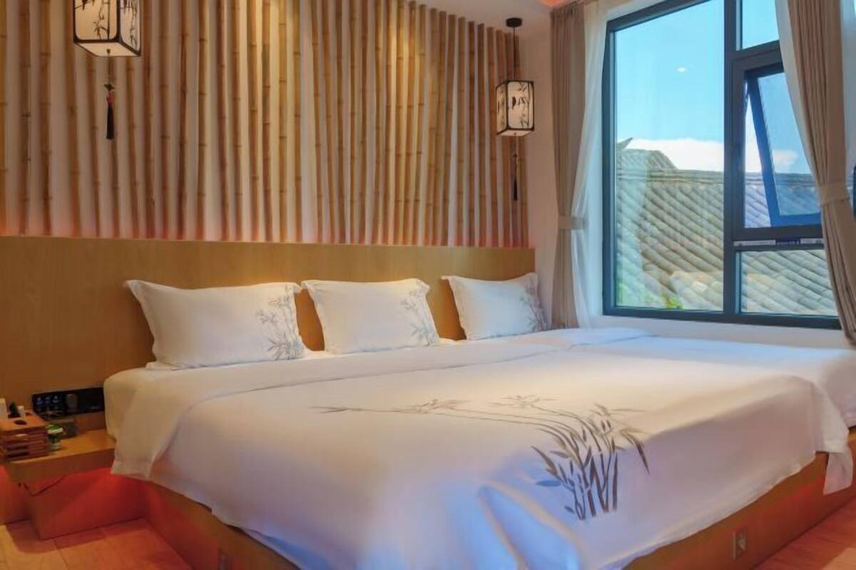 A hotel room with a large bed, a window with a view, and a wall with vertical blinds.