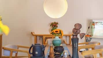 A dining area with a table set for two, a vase with flowers, and a large light fixture above.