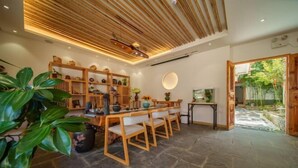 A modern dining area with a wooden ceiling, stone flooring, and a view of a garden through an open door. - Huachengju View Guesthouse (Jianshui)