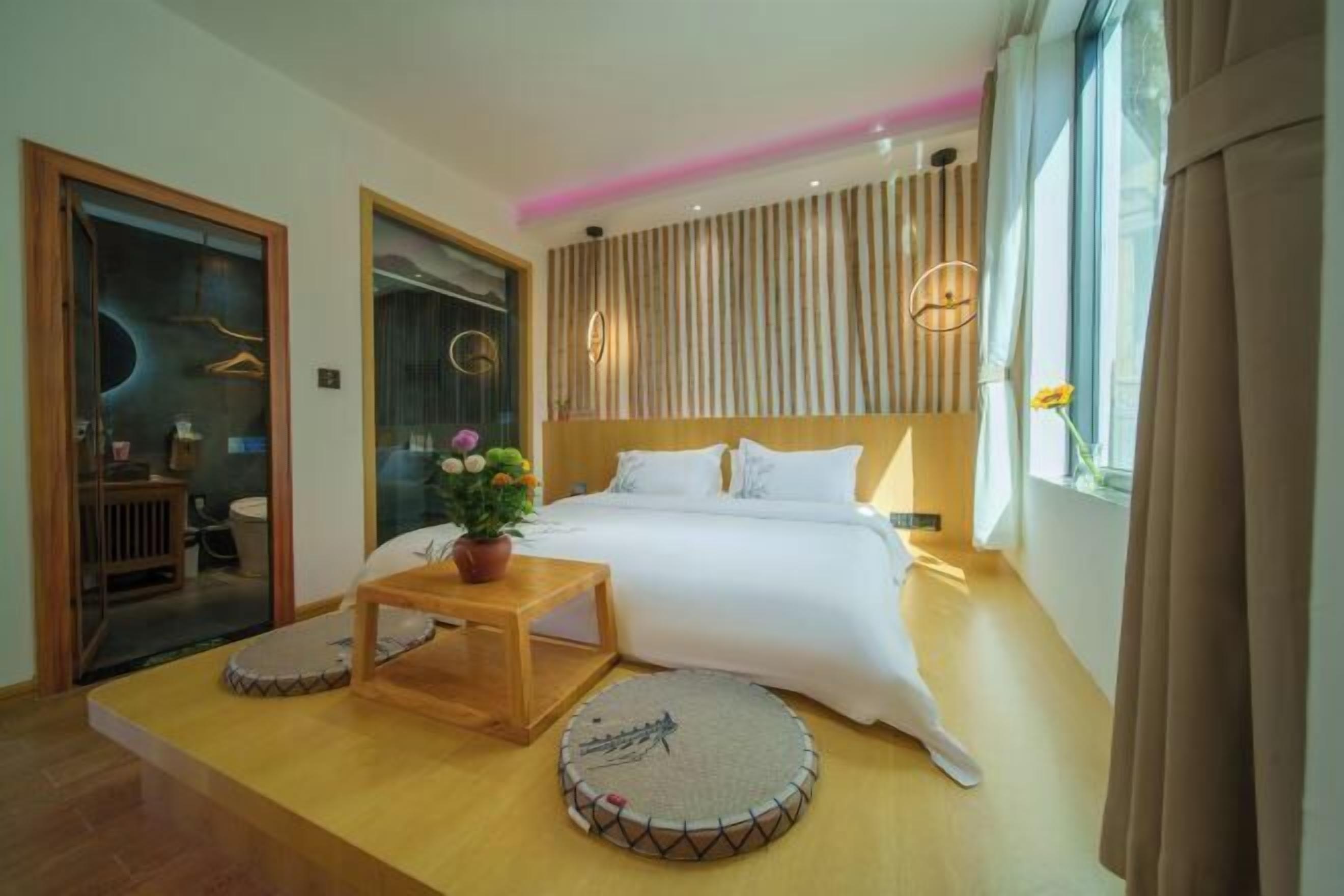 A modern hotel room with a large bed, a small wooden table, a potted plant, and a round rug.