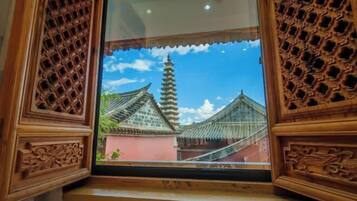 A traditional wooden window with intricate carvings, a clear view of a pagoda-style building, and a blue sky with clouds.