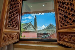 A traditional wooden window with intricate carvings, a clear view of a pagoda-style building, and a blue sky with clouds. - Huachengju View Guesthouse (Jianshui)