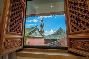 Una ventana de madera tradicional con elaborados grabados, una vista despejada de un edificio de estilo pagoda y un cielo azul con nubes.