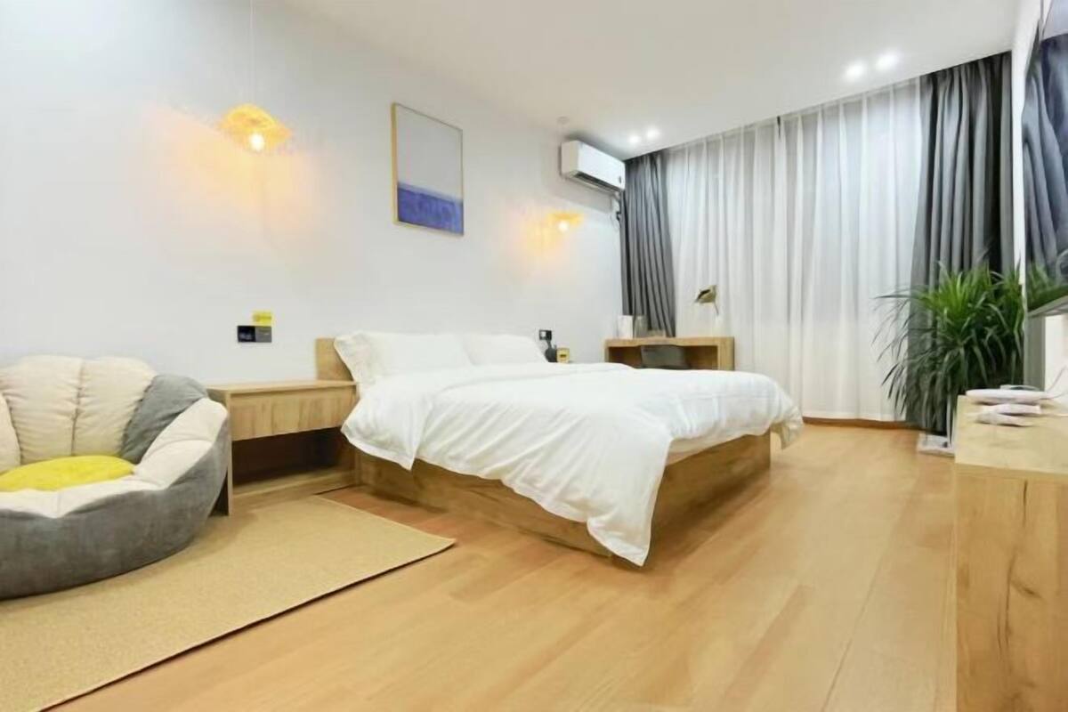 A modern bedroom with a bed, bedside table, lamp, and a potted plant.