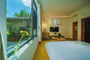 Habitación de hotel moderna con una cama grande, un escritorio, una silla, un televisor y vistas al exterior con zonas verdes.