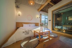 A bedroom with a bed, bedside table, and a view of a balcony. - Huachengju View Guesthouse (Jianshui)